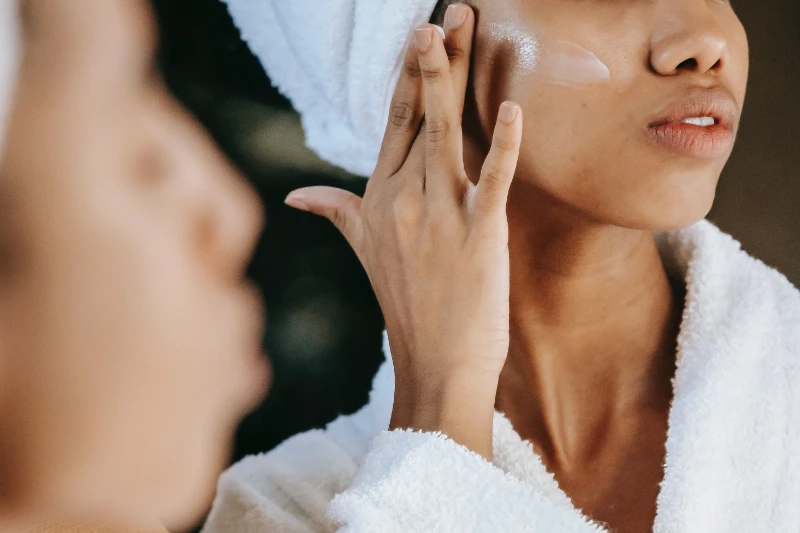 Skin Health - woman in a robe with a towel on her head applying face cream